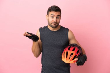 Pembe arka planda izole edilmiş genç bisikletçi ellerini kaldırırken şüpheleri var.