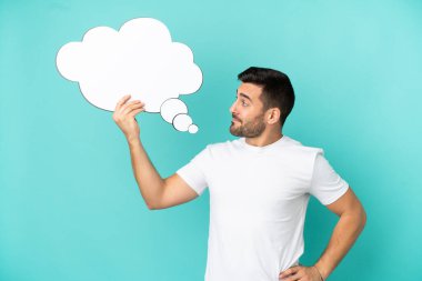 Mavi arka planda izole edilmiş yakışıklı beyaz adam boş bir konuşma balonu tutuyor.