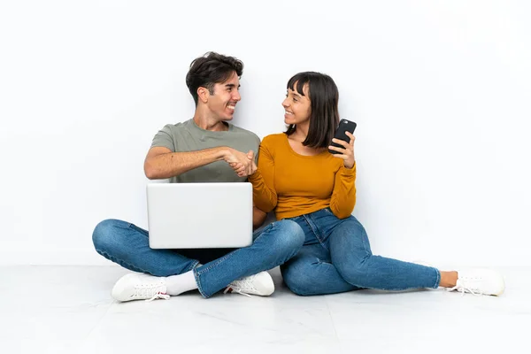 这对年轻夫妇带着笔记本电脑和手机坐在地板上 在经过一番愉快的握手之后 — 图库照片