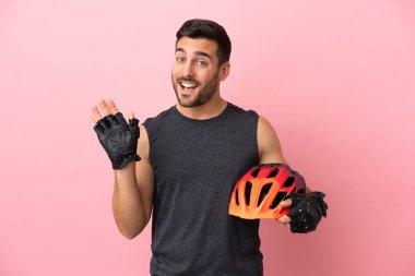Pembe arka planda izole edilmiş genç bisikletçi mutlu bir ifadeyle selamlıyor.