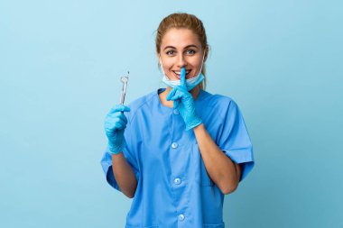 Genç dişçi kadın, mavi arka planda aletleri tutuyor. Sessiz hareketler yapıyor.