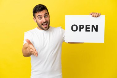 Sarı arka planda izole edilmiş yakışıklı beyaz bir adam. Elinde bir pankartla bir anlaşma yapıyor.