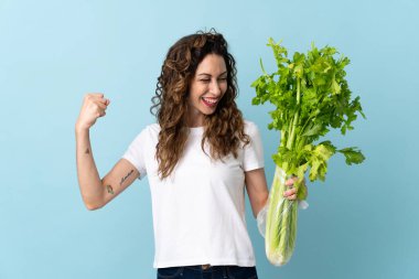 Mavi arka planda izole edilmiş bir kereviz taşıyan genç kadın zaferi kutluyor.