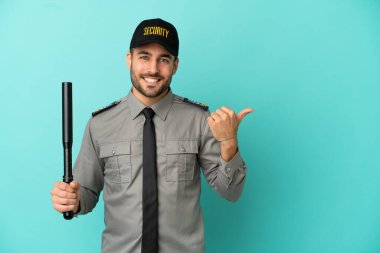 Mavi arka planda izole edilmiş genç bir güvenlik görevlisi bir ürünü sunmak için kenarı işaret ediyor.