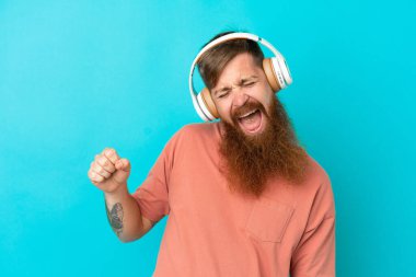 Kırmızımsı beyaz adam mavi arka planda izole edilmiş müzik ve dans dinliyor.