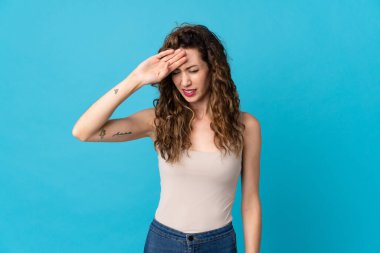 Kafkasyalı genç bir kadın mavi arka planda izole edilmiş, yorgun ve hasta bir ifadeyle.