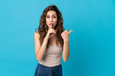 Mavi arka planda izole edilmiş genç, beyaz bir kadın. Yan tarafı işaret ediyor ve sessiz hareketler yapıyor.
