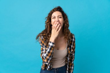 Mavi arka planda izole edilmiş genç beyaz kadın mutlu ve gülümsüyor.