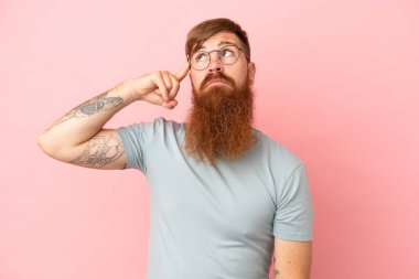 Pembe arka planda izole edilmiş genç, beyaz bir adam deliliğin jestini yapıyor. Parmağını kafaya koyuyor.