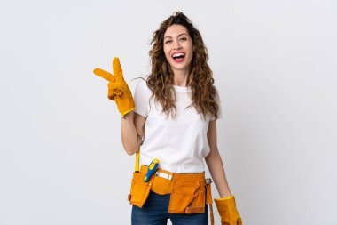 Beyaz arka planda izole edilmiş genç elektrikçi gülümsüyor ve zafer işareti gösteriyor.