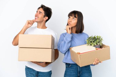 Genç çift, beyaz arka planda izole edilmiş eşyalarla dolu bir kutuyu alıp yukarı bakarken bir fikir üretiyor.