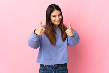 Pembe arka planda izole edilmiş beyaz bir kadın baş parmak hareketi yapıyor.