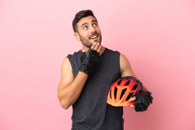 Pembe arka planda izole edilmiş genç bisikletçi gülümserken yukarı bakıyor