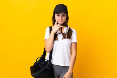 Spor çantalı genç bir kadın sarı arka planda izole edilmiş ve düşünüyor.
