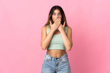Pembe arka planda izole edilmiş genç beyaz kadın elleriyle ağzını kapatıyor.