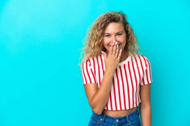 Mavi arka planda izole edilmiş kıvırcık saçlı mutlu ve gülümseyen eli ağızlı bir kız.