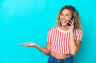 Kıvırcık saçlı kız mavi arka planda izole edilmiş cep telefonuyla biriyle sohbet ediyor.