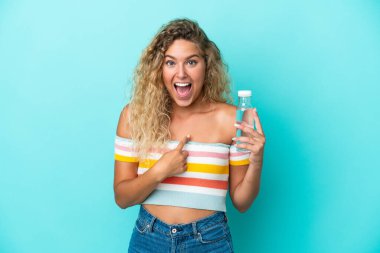 Mavi arka planda su şişesi olan sarışın genç bir kadın. Şaşırtıcı bir yüz ifadesi var.