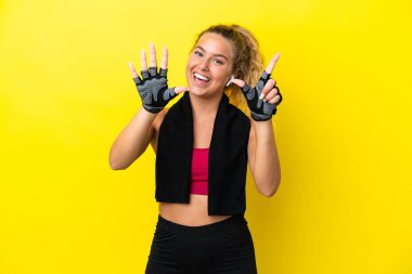 Sarı arka planda izole edilmiş havlusu olan sporcu kadın yediyi parmaklarıyla sayıyor