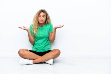 Kıvırcık saçlı kız yerde oturuyor ve ellerini kaldırırken şüphe duyuyor.