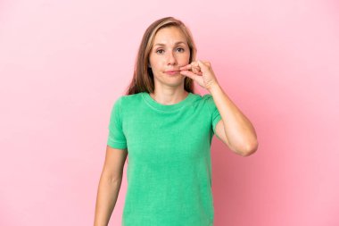 Pembe arka planda izole edilmiş genç bir İngiliz kadın sessizlik işareti gösteriyor.