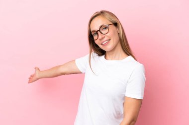 Pembe arka planda izole edilmiş genç bir İngiliz kadın davet edildiği için ellerini yana uzatıyor.