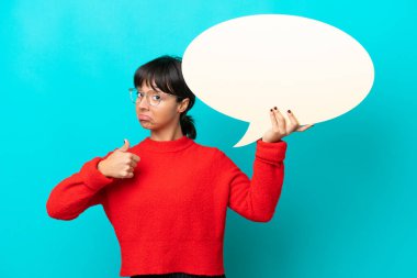 Mavi arka planda izole edilmiş genç bir kadın başparmağıyla boş bir konuşma balonu tutuyor.