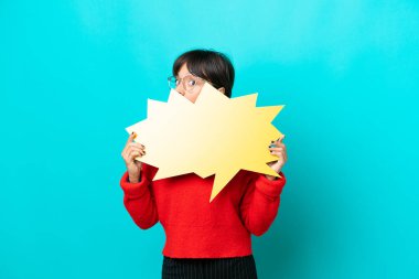 Mavi arka planda izole edilmiş genç bir kadın boş bir konuşma balonu tutuyor ve arkasında saklanıyor.