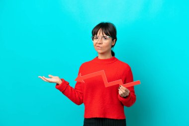 Mavi arka planda izole edilmiş genç bir kadın aşağıya doğru bir ok tutuyor ve üzgün bir ifadeyle