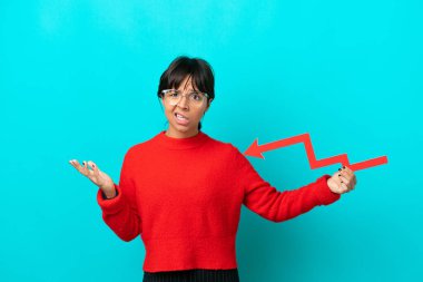 Mavi arka planda izole edilmiş genç bir kadın aşağıya doğru bir ok tutuyor ve üzgün bir ifadeyle