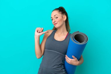 Genç beyaz kadın yoga derslerine giderken elinde mavi arka planda kendini beğenmiş ve gururlu bir minder tutuyordu.