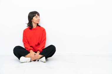 Genç melez kadın, beyaz arka planda izole bir şekilde yerde oturuyor.