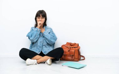 Beyaz arka planda zemin katta oturan genç bayan öksürükten ve kötü hissetmekten muzdarip.