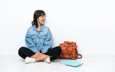 Genç bir kız öğrenci beyaz arka planda tek başına oturuyor. Yan pozisyonda gülüyor.