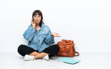 Beyaz arka planda zemin katta oturan genç bir bayan cep telefonuyla sohbet ediyor.