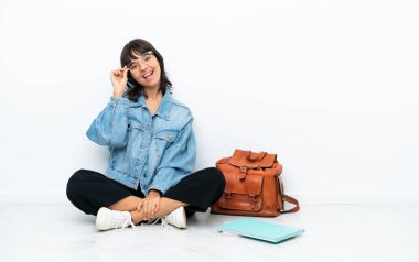 Genç bayan, beyaz arka planda gözlüklü ve mutlu bir şekilde zemin katta oturuyor.