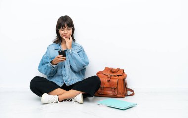 Genç bir kız öğrenci beyaz arka planda tek başına oturuyor. Düşünüyor ve mesaj yolluyor.