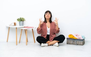Genç melez kadın, katlanan giysiler katlıyor. Zen pozunda beyaz arka planda izole bir şekilde yerde oturuyor.