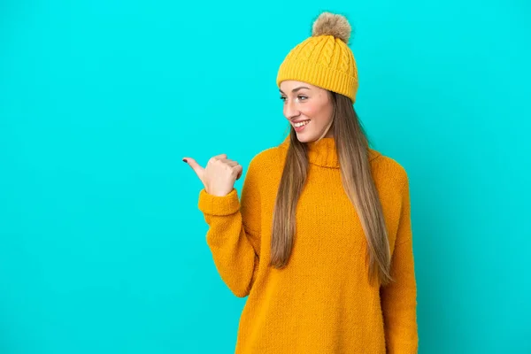 冬のジャケットを身に着けている若い白人女性は 製品を提示するために側面を指す青い背景に隔離されています — ストック写真