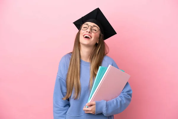 若いです学生女性身に着けていますA大学の帽子絶縁上のピンクの背景笑い — ストック写真