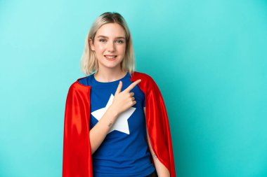 Süper Kahraman Kafkas kadın, mavi arka planda izole edilmiş bir şekilde bir ürün sunmak için kenarı işaret ediyor.