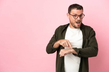 Pembe arka planda izole edilmiş genç Brezilyalı adam geç kalma jesti yapıyor.