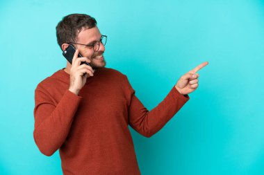 Mavi arka planda izole edilmiş cep telefonu kullanan genç Brezilyalı bir adam parmağını yana uzattı ve bir ürün sundu.