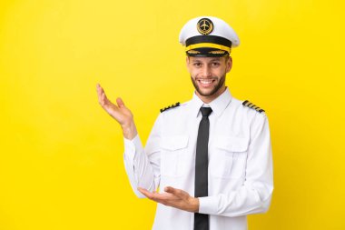Kafkasyalı uçak pilotu sarı arka planda izole edilmiş ve davet edilmek üzere ellerini yana uzatıyor.