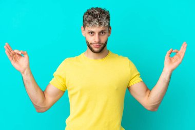 Zen pozunda mavi arka planda izole edilmiş yakışıklı beyaz bir adam.