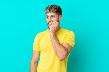 Mavi arka planda izole edilmiş yakışıklı beyaz adam biraz gergin.