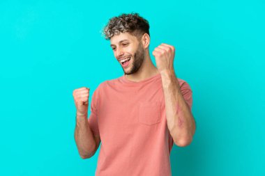 Mavi arka planda izole edilmiş yakışıklı beyaz adam zaferi kutluyor.