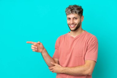 Genç, beyaz, mavi arka planda izole edilmiş ve parmağını yana doğru gösteren bir adam.