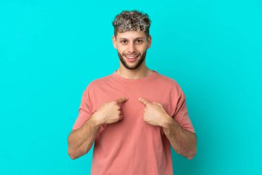 Mavi arka planda mahsur kalmış yakışıklı, beyaz bir adam. Şaşırtıcı bir yüz ifadesi var.