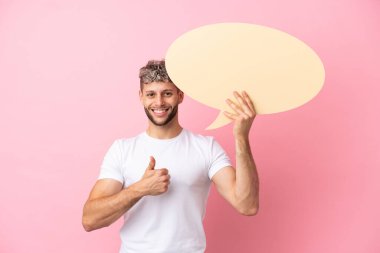 Pembe arka planda izole edilmiş yakışıklı beyaz bir adam boş bir konuşma balonunu başparmağıyla havada tutuyor.